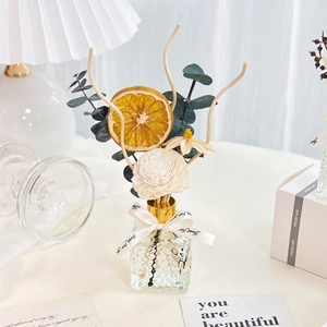 Detailed set of reed diffuser with eucalyptus, orange slice, and glass bottle on desk