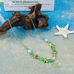 Macro detail of gold necklace with green stones, starfish and seashell charms on beach sand