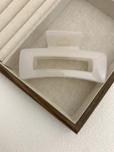 Detailed view of a creamy white rectangular claw clip placed on a fabric jewelry tray