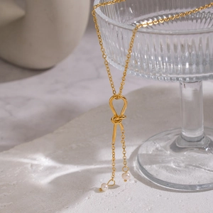 Elegant gold sweater chain with knot tassel and natural freshwater pearls on glass