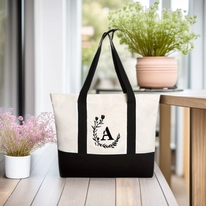 Outdoor close-up of a cream canvas tote bag with black handles and floral letter A print
