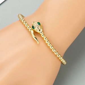 Macro shot of gold snake bracelet with green emerald eyes and white zircon inlay