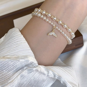Detail of double-layer pearl bracelet featuring a sparkling gold fishtail charm on wrist
