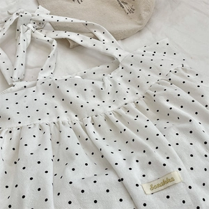 Detailed close-up of white polka dot fabric with pleated bust and adjustable bow straps