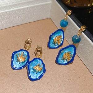 Détail de boucles d'oreilles fleurs en émail bleu et pendants à perles sur velours
