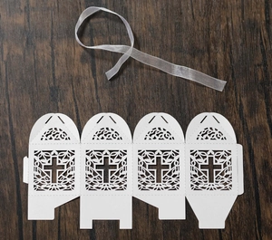 Flat lay of laser-cut white cardstock candy box featuring cross motif and organza ribbon