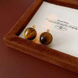 Gros plan de boucles d'oreilles en œil de tigre doré sur fond vintage français