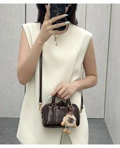 Detail of dark brown mini Boston bag with gold hardware and plush sheep charm accessory