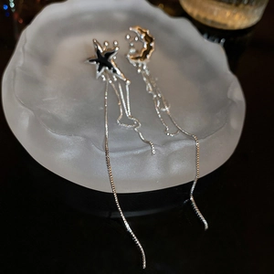 Détail de boucles d'oreilles à pampilles lune et étoile en argent sur un plateau blanc mat