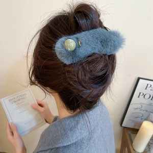 Detail of grey-blue plush hair claw clip with green bead on model in cozy home setting