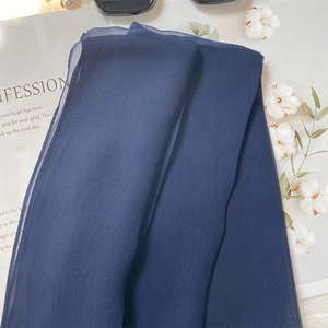 Detail of navy blue silk scarf with fine texture folded on a magazine with sunglasses
