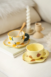 Detail of cute hand-painted ceramic coffee cups with lemon and bear patterns and saucers
