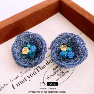 Blue woven flower stud earrings with three-color gemstone center on retro background