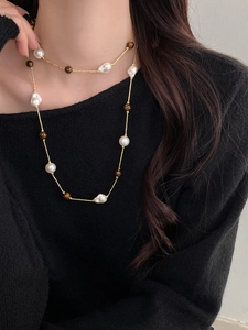 Detail of tiger eye and irregular pearl necklace on black sweater for elegant styling
