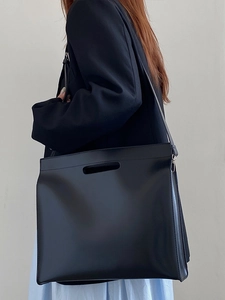 Detail of a black leather tote bag with sturdy handles and adjustable shoulder strap