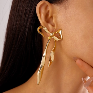 Détail de boucles d'oreilles nœud en métal doré portées sur modèle pour un style chic