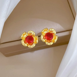 Detailed macro view of golden flower earrings featuring central red round gemstones