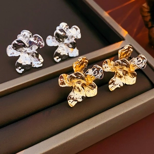 Close-up of irregular metal flower stud earrings in gold and silver with lava texture