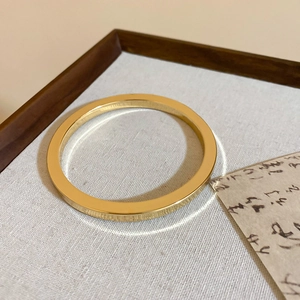 Minimalist gold bangle with flat rectangular profile on elegant calligraphy backdrop