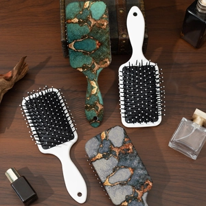 Square cushion hairbrushes with elegant marble pattern handles on a wooden background