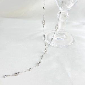 Silver coffee bean link necklace with zircons draped over a glass on white silk