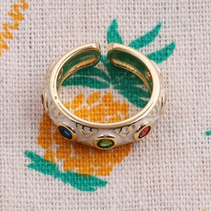 Detail of adjustable gold-plated ring with white enamel and colorful inset gemstones