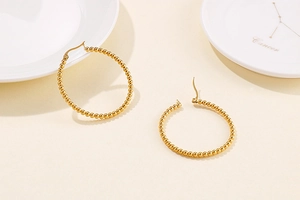 Detail of gold beaded hoop earrings featuring a textured sphere design on a ceramic plate