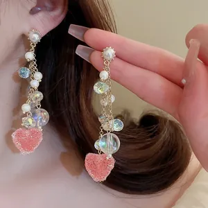 Close-up of dangling earrings with white pearls and a pink frosted heart pendant