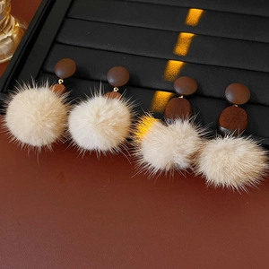 Close-up of retro wooden earrings with fur balls on a premium brown leather background