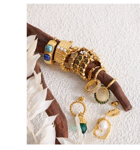 Close-up of gold-plated U-shaped twist earrings and green zircon rings on a wooden branch