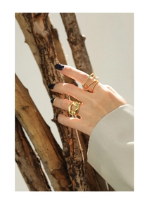 Detail of gold chain link and spiral rings on hand with a rustic branch backdrop