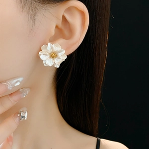 Detail of white resin flower earring with golden stamen worn by model on black background