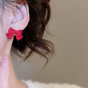 Detailed close-up of a matte red bow-knot stud earring on a female model