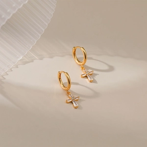Close-up of gold cross earrings with baguette-cut zircon stones on a minimal surface