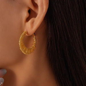 Close-up of golden geometric mesh textured hoop earring worn on a model's ear