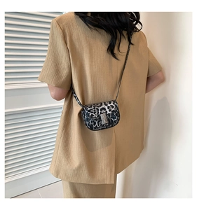 Detail of leopard print crossbody bag with silver buckle worn over a beige suit