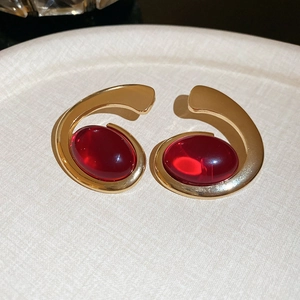 Detail of gold oval earrings with deep red resin gemstones and a metallic finish