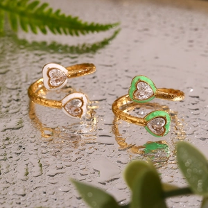 Detail of 18K gold plated heart rings with green and white enamel on a water-drop surface