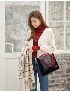 Detail of a black embossed tote bag with red handles held by a fashion model indoors