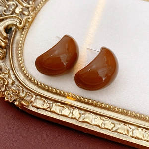 Brown C-shaped resin stud earrings displayed on a vintage gold frame with red leather
