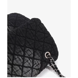 Close-up of black quilted denim fabric texture and silver metal chain strap detail
