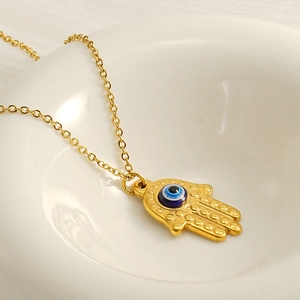 Gold Hamsa Hand necklace with blue evil eye pendant displayed in a white ceramic bowl