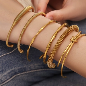 Stack of gold bamboo-style and textured stainless steel bracelets on a model