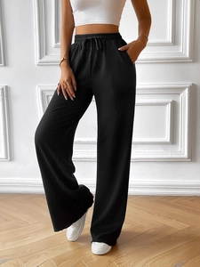 Detail showing the elastic high waist with adjustable drawstring on black wide-leg trousers