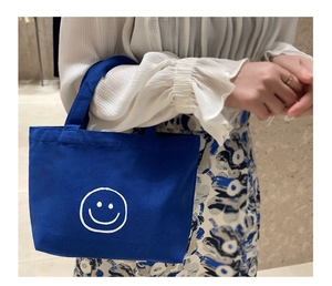 Detail of Klein blue canvas handbag with white smiley face and reinforced handles