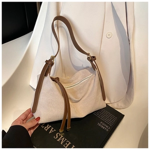 Detailed close-up of a beige faux suede shoulder bag with brown leather fringe and strap