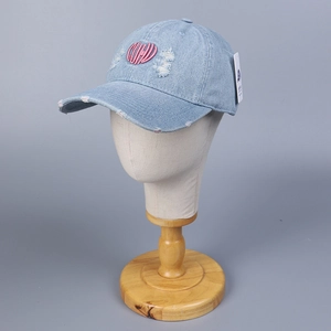 Detail of distressed light blue denim baseball cap with pink heart embroidery and frayed holes