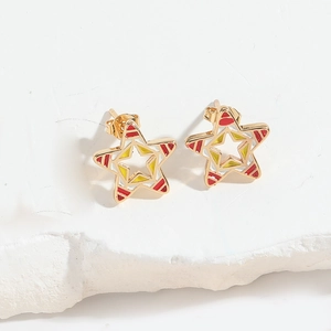 Macro shot of gold star stud earrings with red and yellow enamel on white marble background