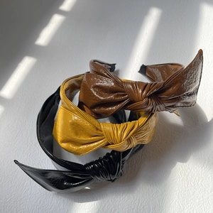 Three retro PU leather bow headbands in black, brown, and yellow with wide knotted design
