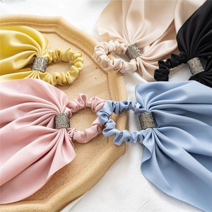 Flat lay of five colorful satin bow hair scrunchies with sparkling rhinestone ring center